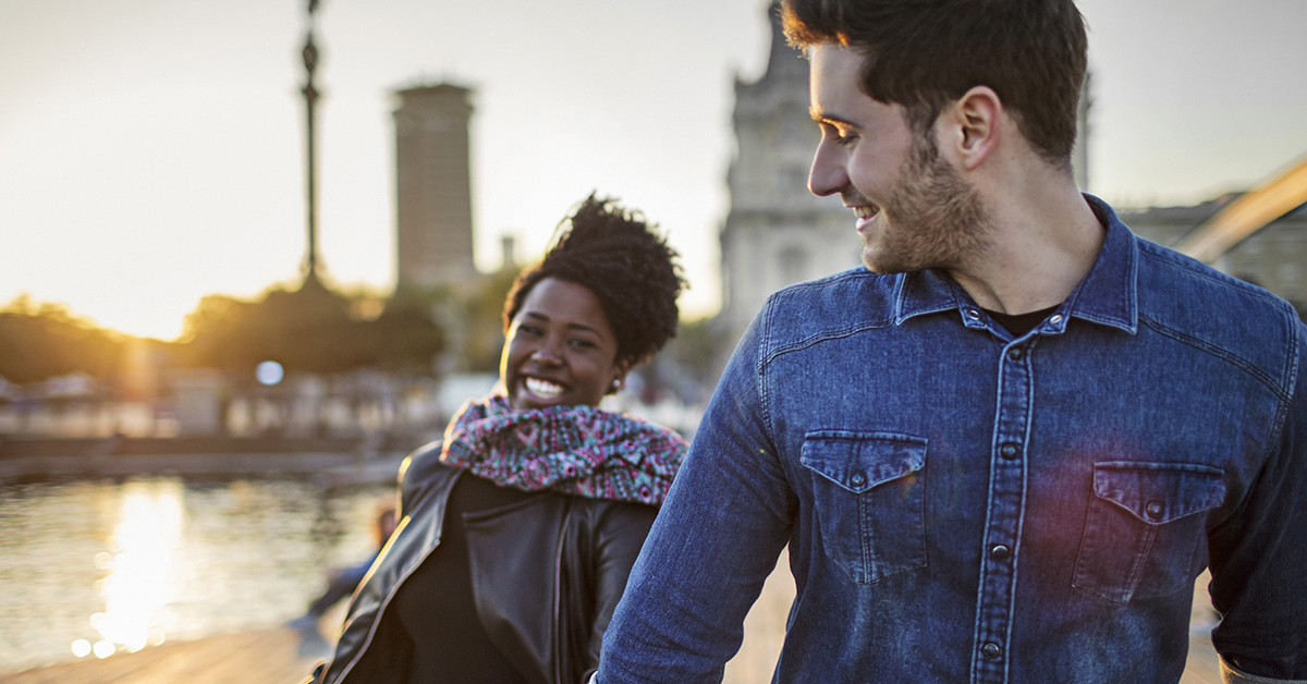 Happy man walking with woman on boardwalk. Multi-ethnic couple are wearing casuals. They are hanging out in city.