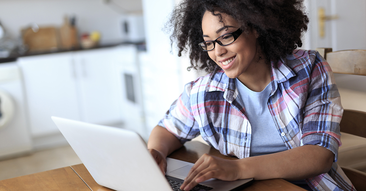 Smiling woman with eyeglasses using laptop at home.