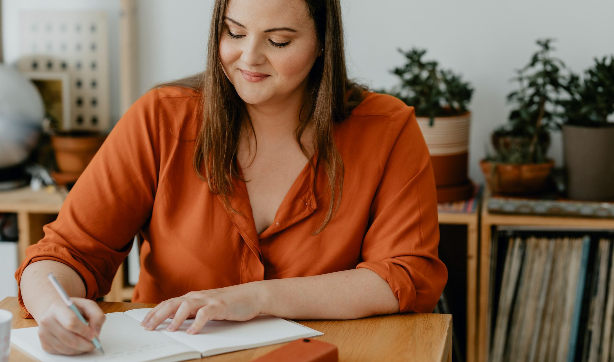 A woman sitting and creating a list in a notebook.