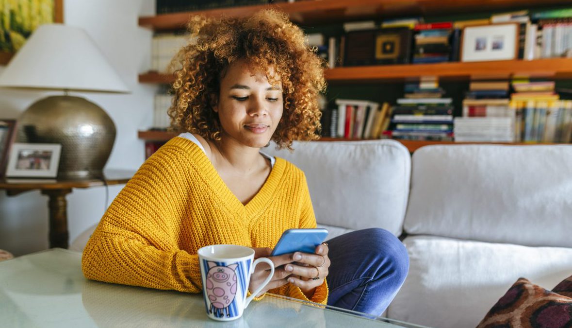 Young woman with curly hair using cell phone at home