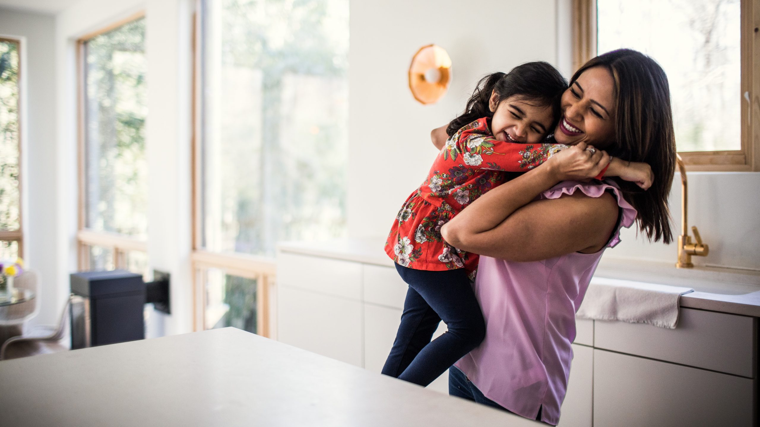 Mother and daughter embracing in kitchen.