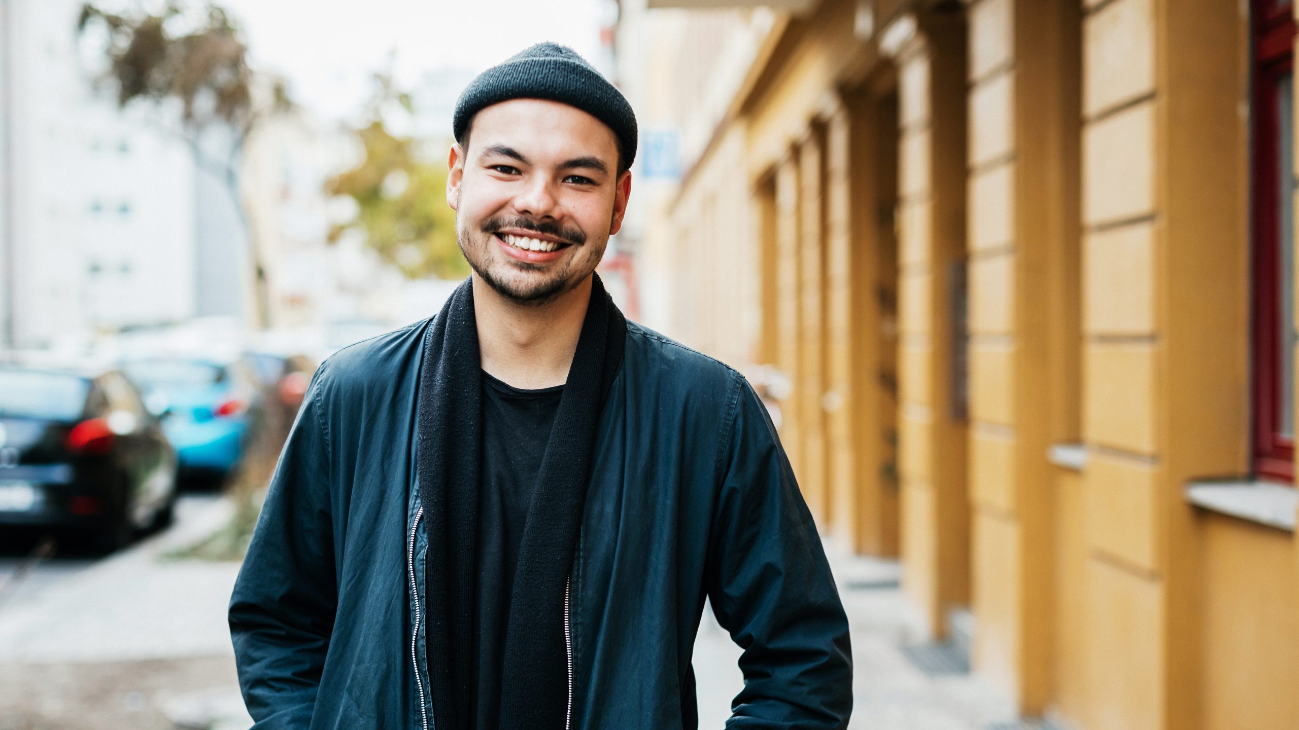 A portrait of a stylish young man standing in a city street, smiling.