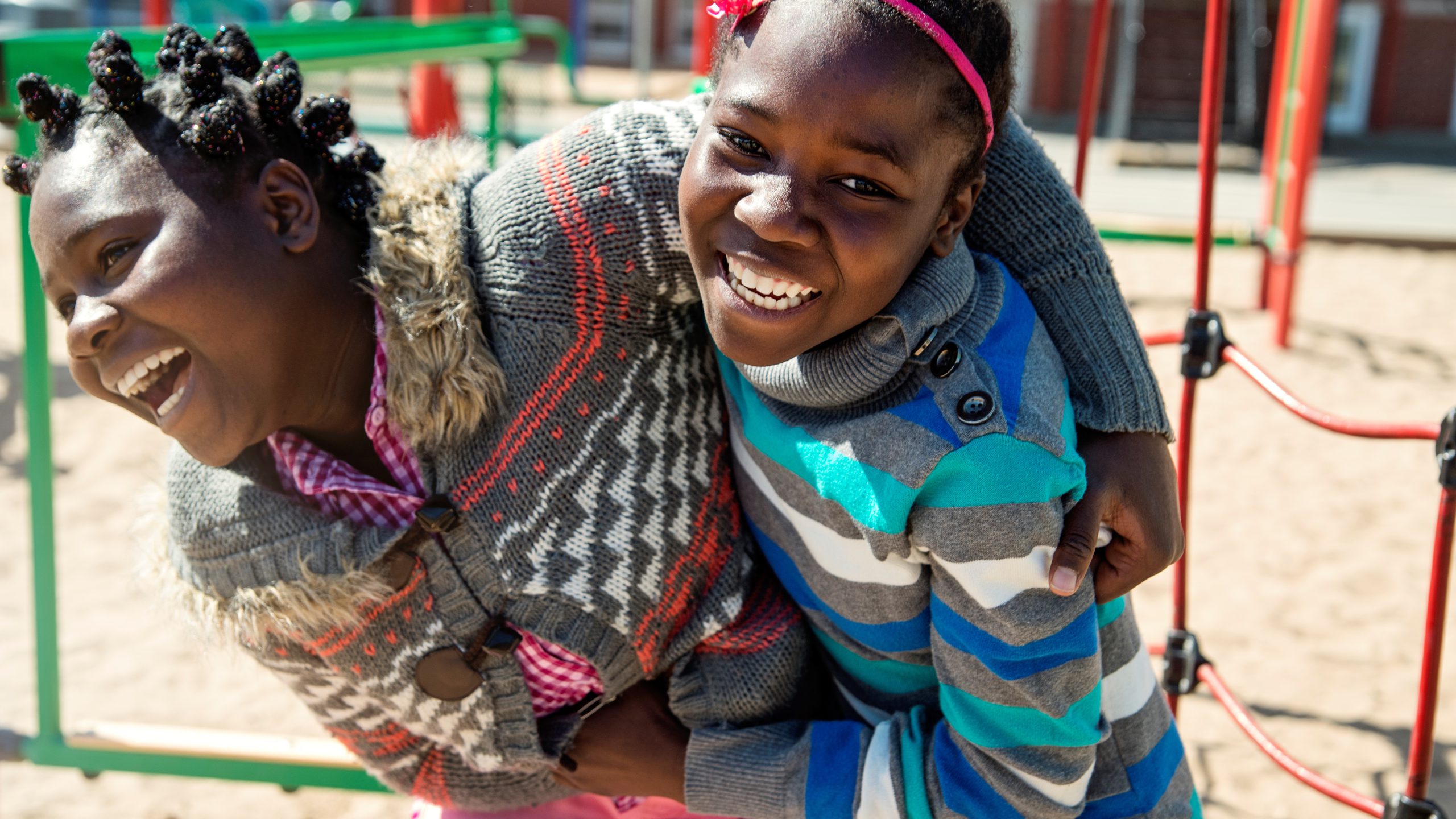 African-Americas preteen twin girls of elementary age active in playground at recess playing together. School in the background. Very sunny mid-season day. Horizontal waist up outdoors shot on a bright sunny day with copy space.