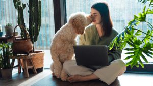 Remote worker sitting on the floor with her laptop and getting sniffed by her dog