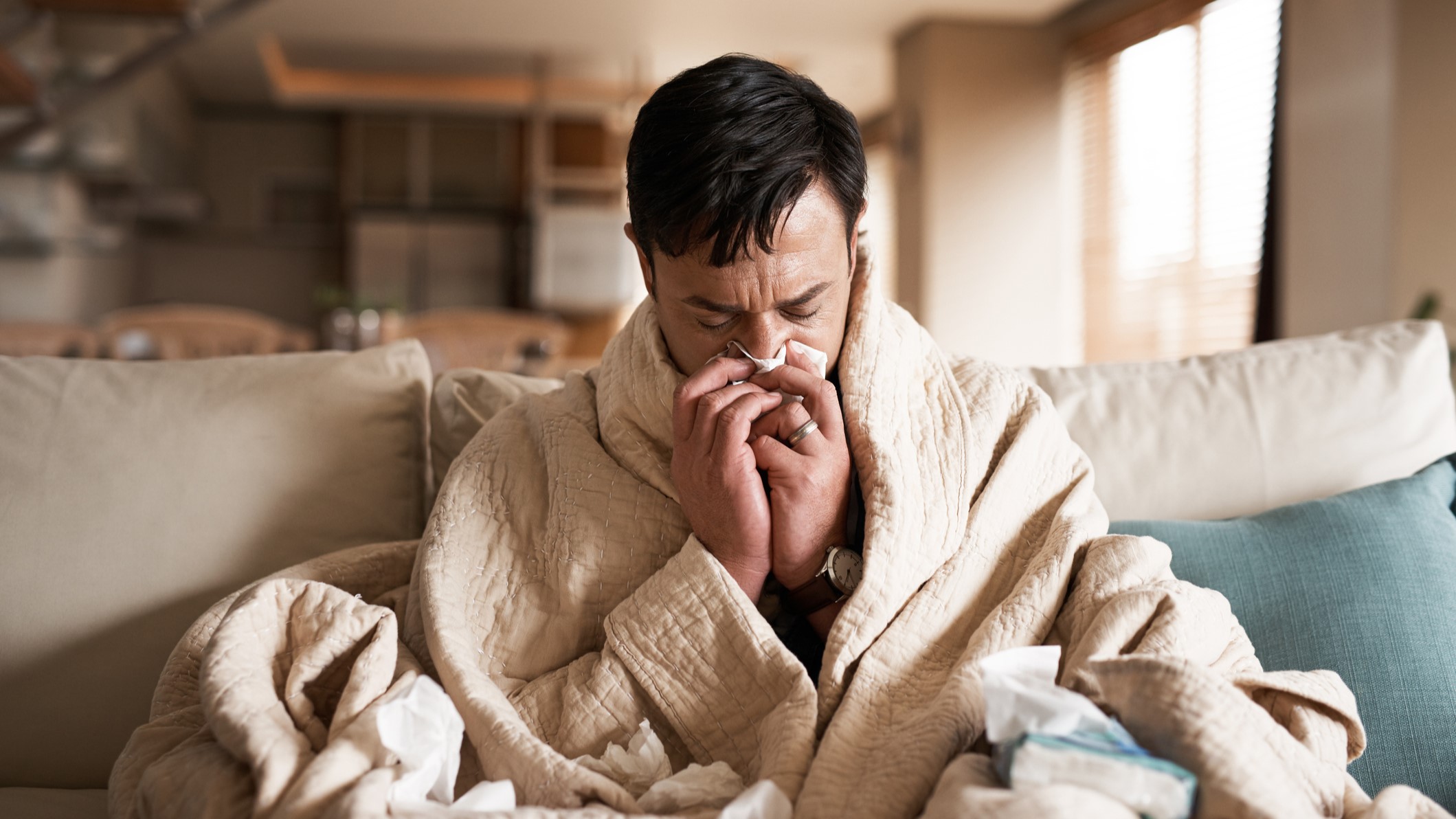 Man wearing a bath robe blowing his nose